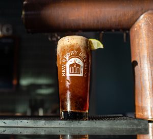 Professional product shot of a dark beer in a tall glass with a lime wedge on a metal bar.