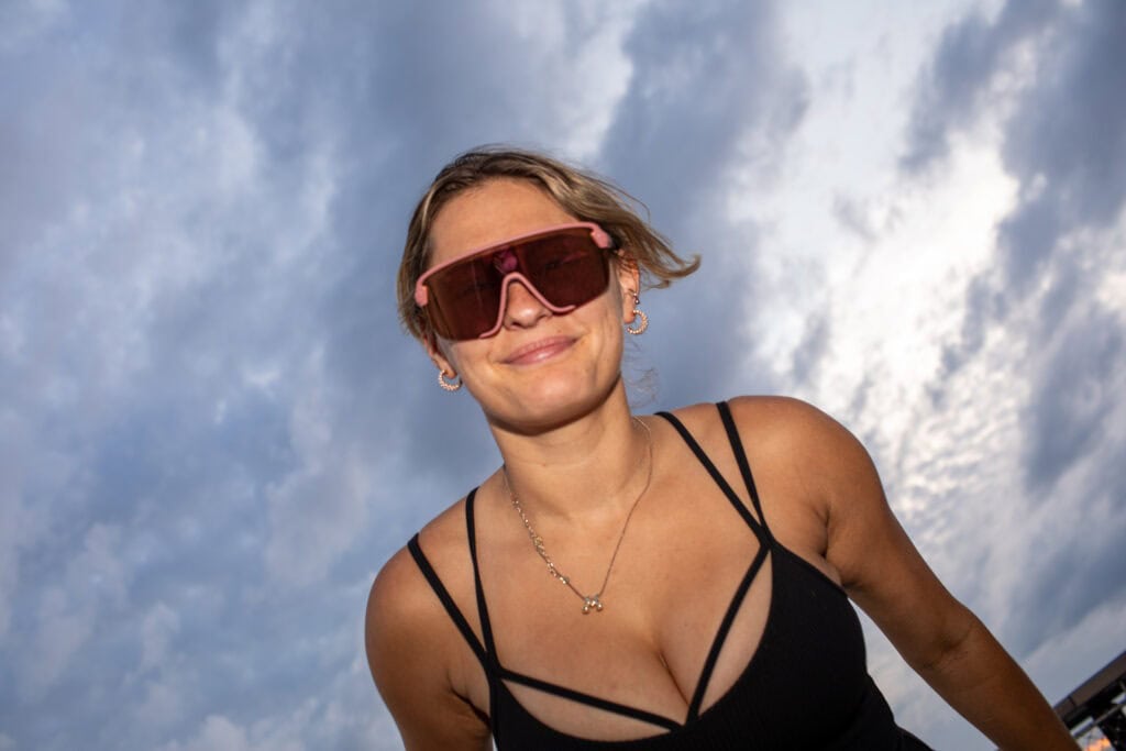 Woman in oversized sunglasses smiling under dramatic clouds