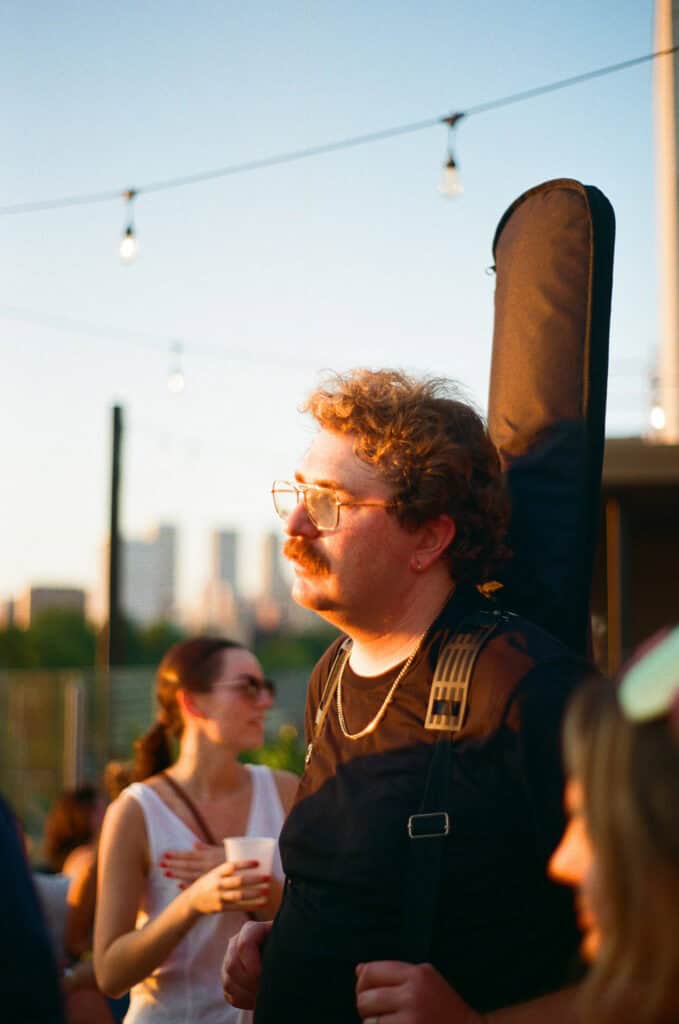 Man carrying a guitar case at a rooftop gathering at sunset