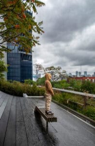 Person in hoodie standing on park bench with cityscape background.