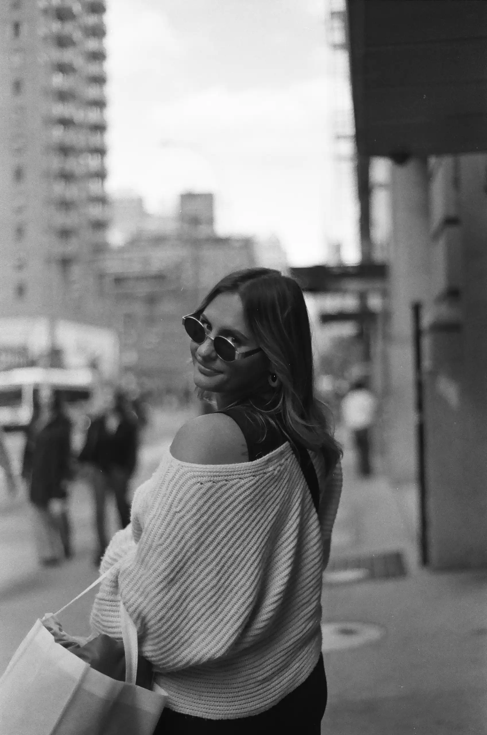 Stylish woman wearing sunglasses and a cozy sweater, enjoying a sunny day in downtown Oklahoma City.