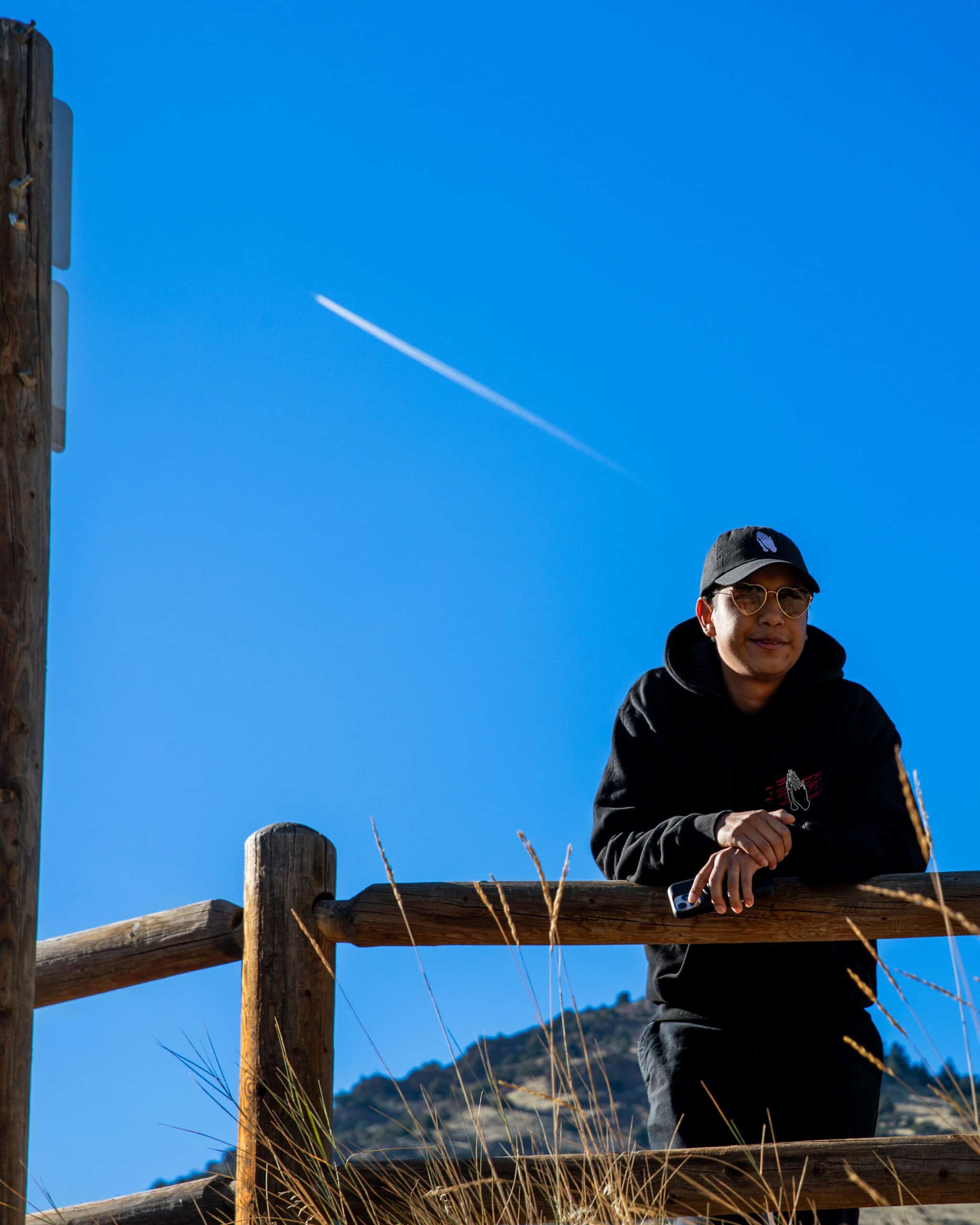 Portrait of a man in a black hoodie and cap outdoors against a clear blue sky.