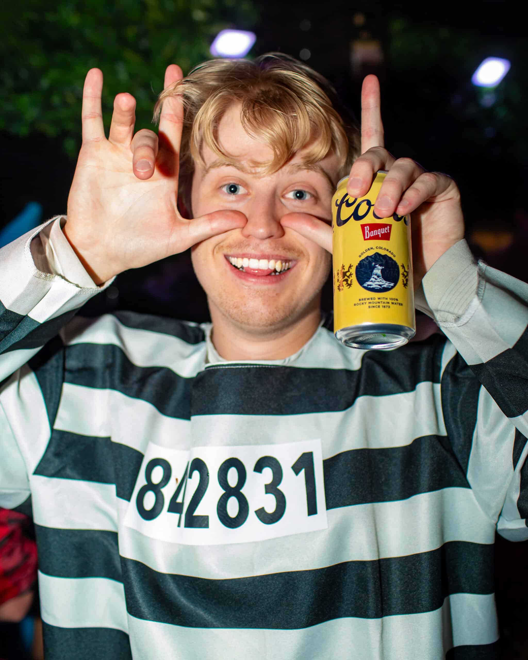 Young man smiling and holding a beer can at a nighttime outdoor event.