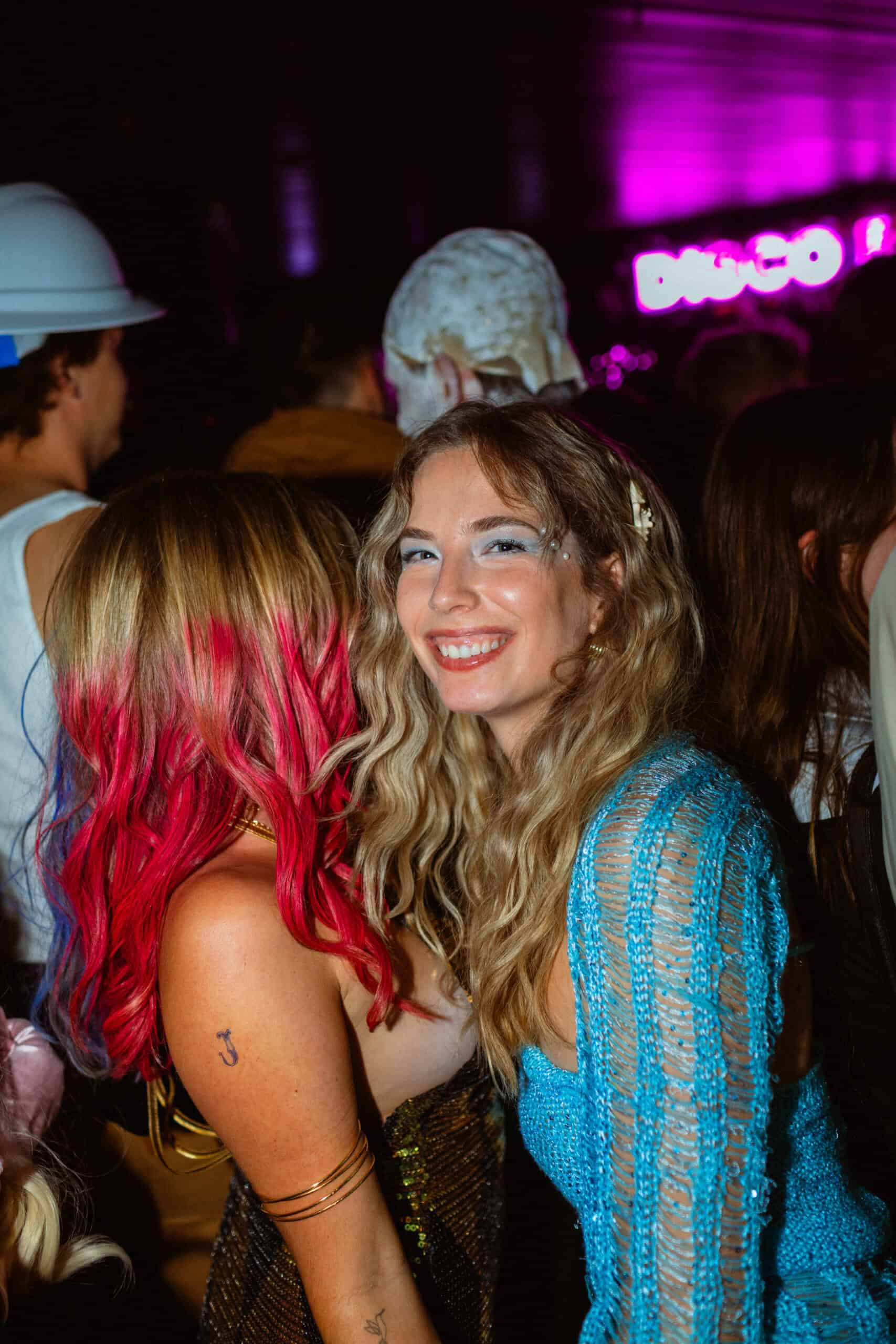 Happy young woman with wavy blonde hair and blue eyeshadow at a lively party.