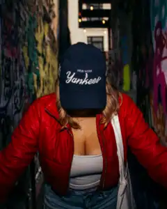Woman wearing a Yankees cap and red jacket in graffiti alleyway.
