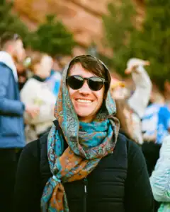 Portrait of a smiling woman with sunglasses and a colorful scarf outdoors.