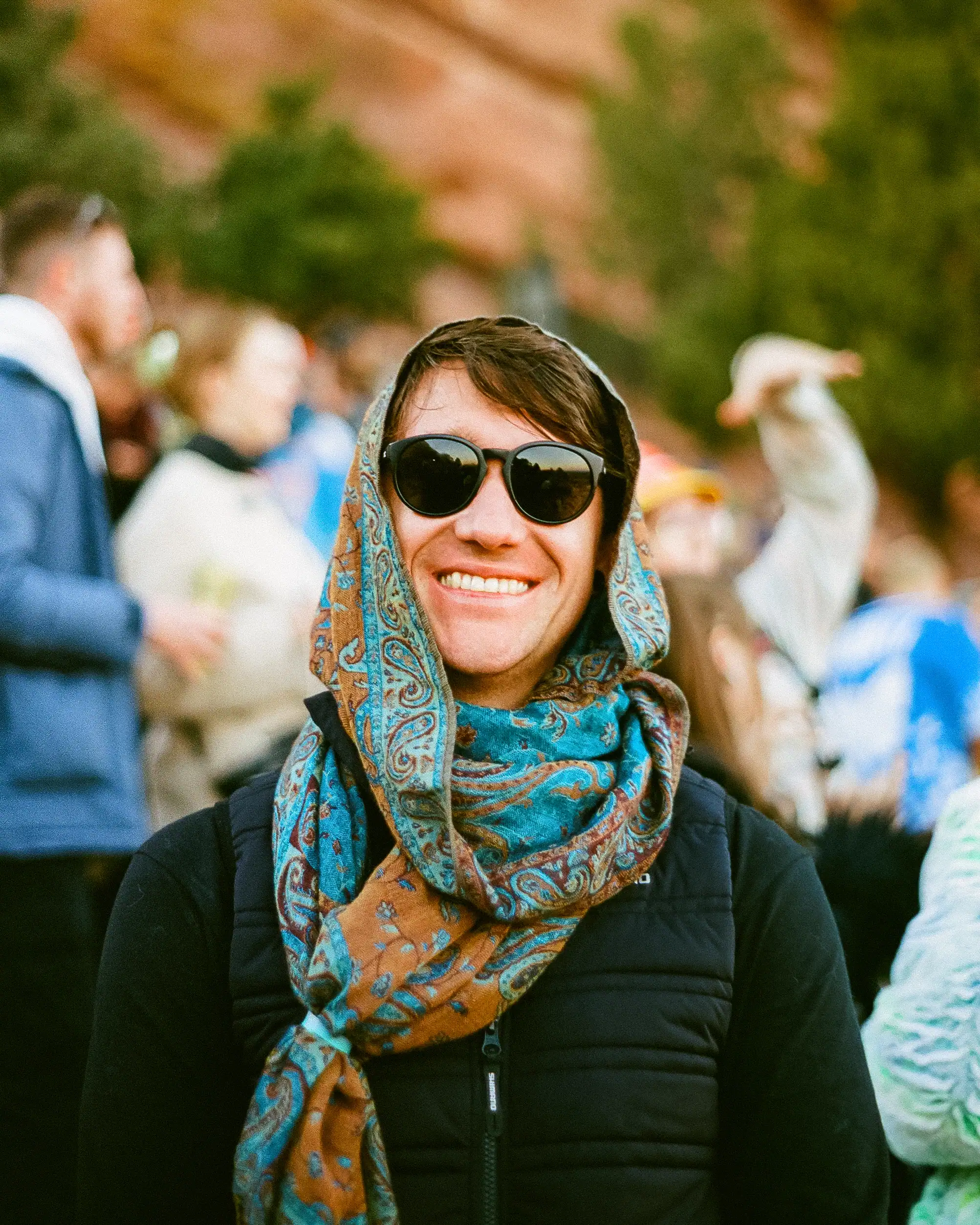 Portrait of a smiling woman with sunglasses and a colorful scarf outdoors.