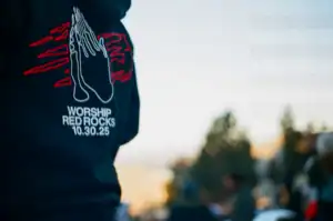 Praying hands graphic on black shirt with "Worship Red Rocks 10.30.25" text.