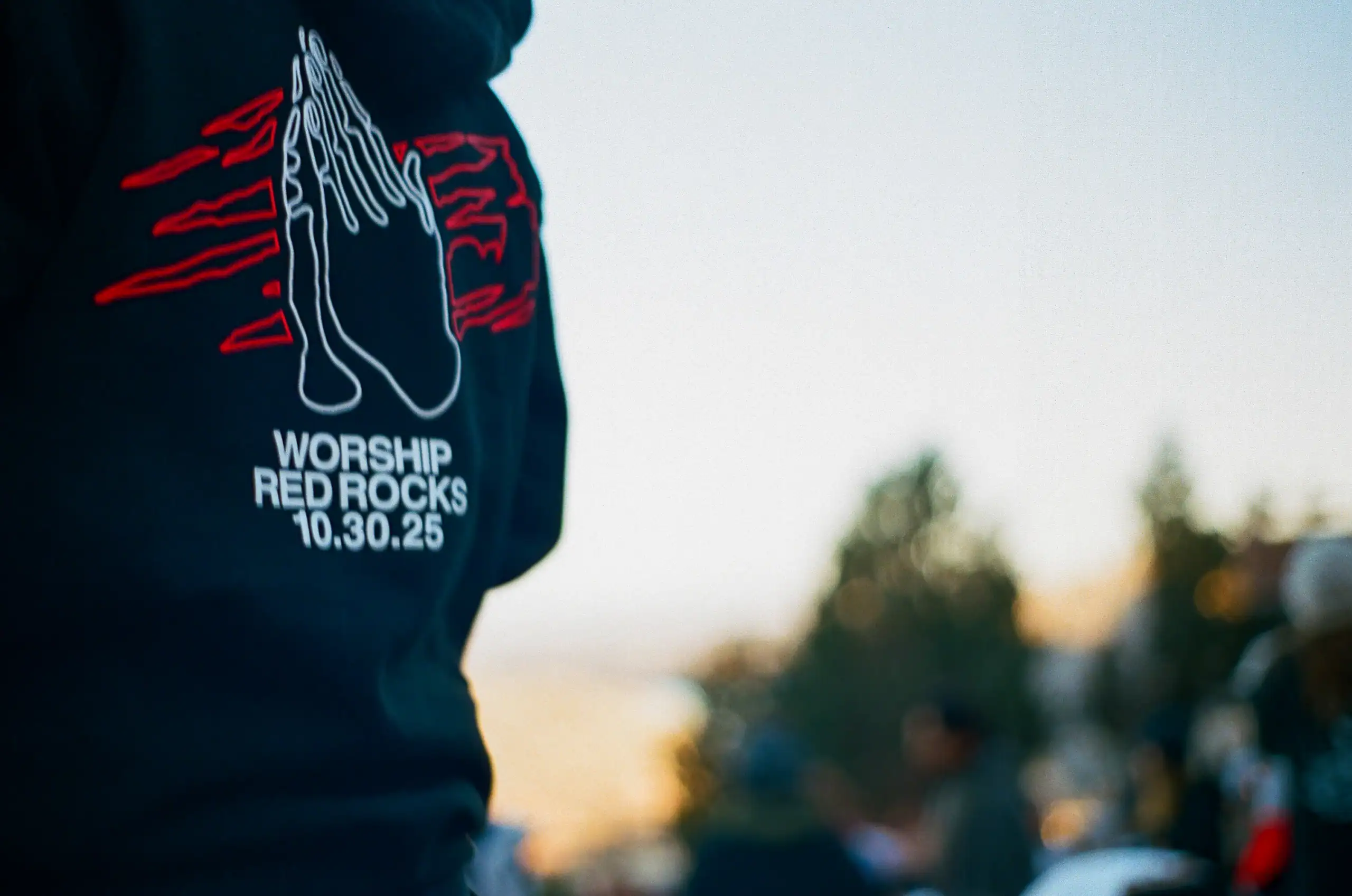 Praying hands graphic on black shirt with "Worship Red Rocks 10.30.25" text.