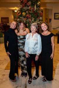 Family portrait with four women standing in front of a decorated Christmas tree in an indoor setting.