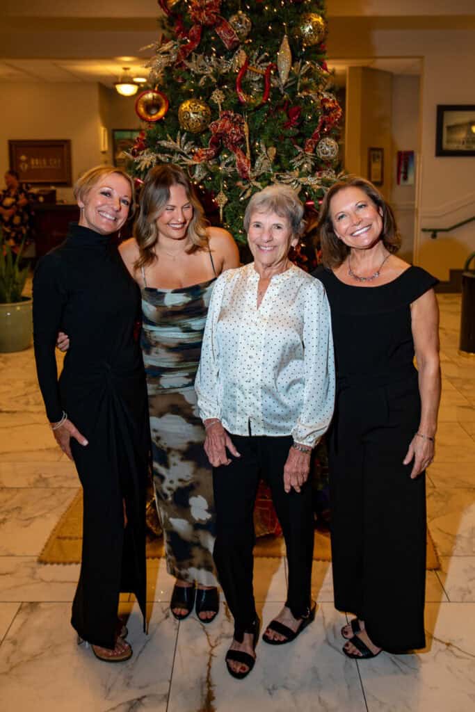 Family portrait with four women standing in front of a decorated Christmas tree in an indoor setting.