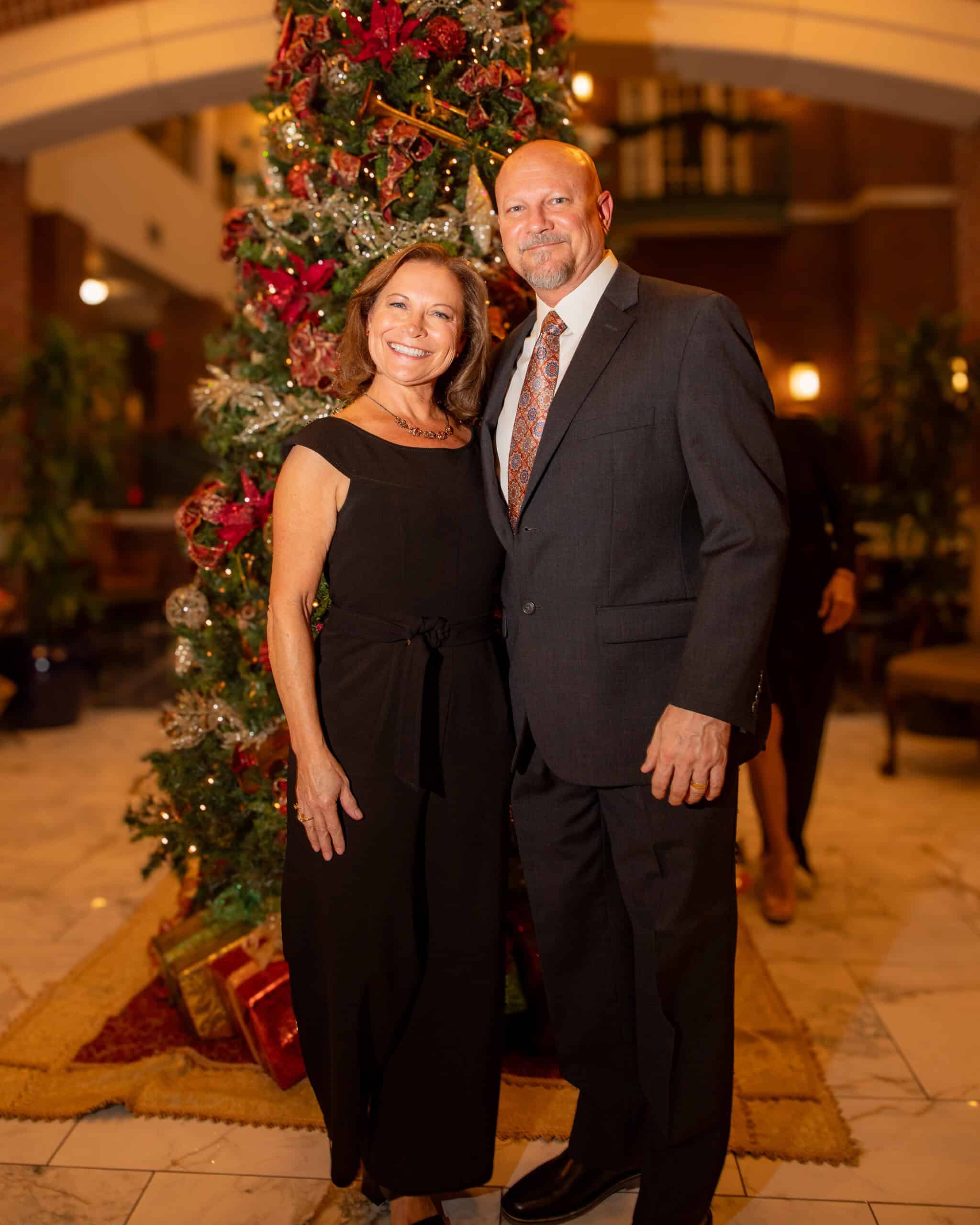 Christmas couple portrait in front of a decorated Christmas tree at an indoor event.