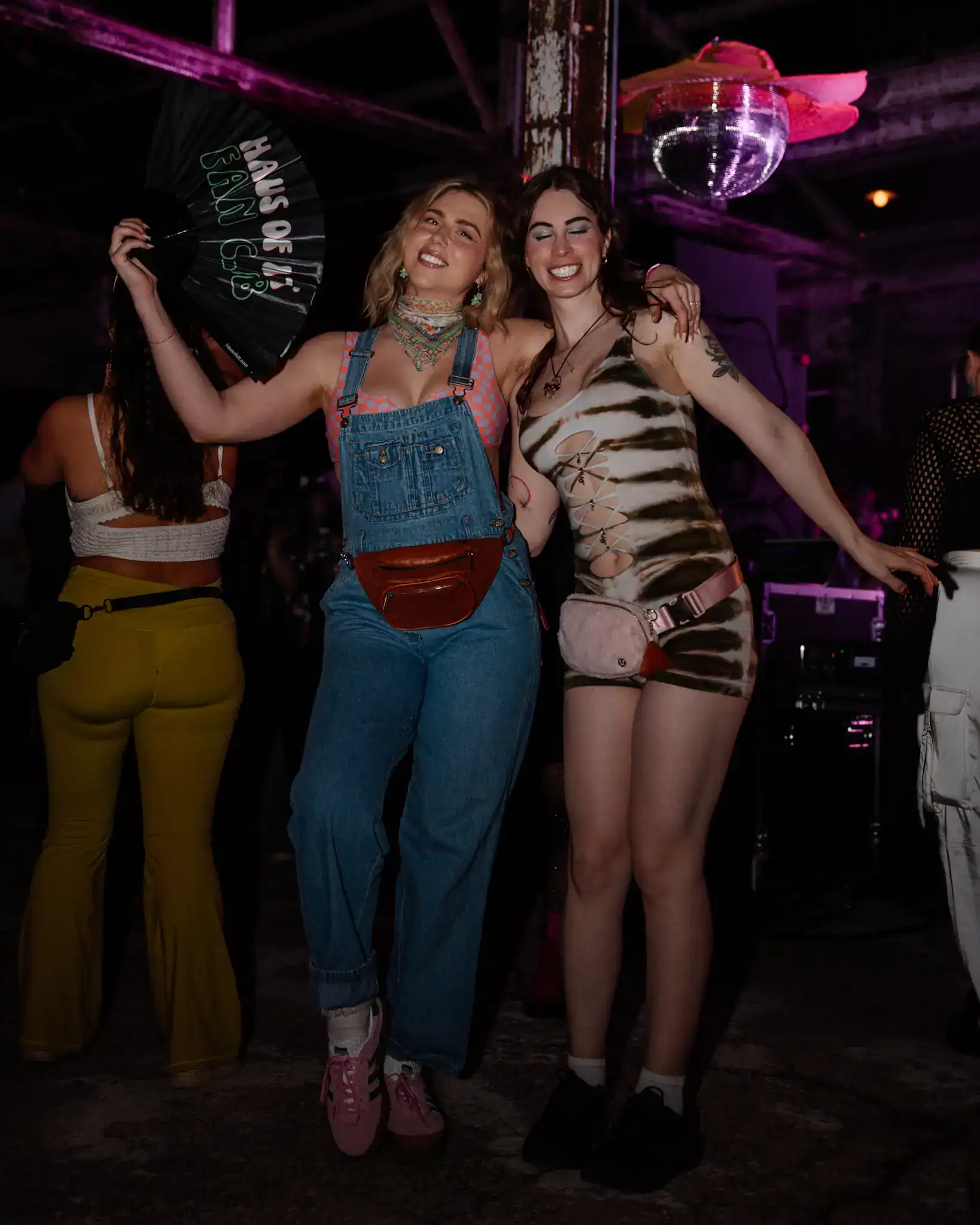 Two women smiling and dancing at a party, enjoying a fun night out with vibrant lighting.
