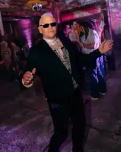 Elegant man dancing at a lively party in a dimly lit venue.