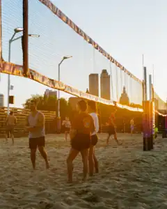 Oklahoma volleyball game at sunset with players and city skyline.