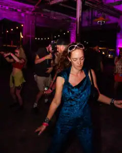 Vibrant woman dancing at an indoor event with colorful lighting and lively atmosphere.
