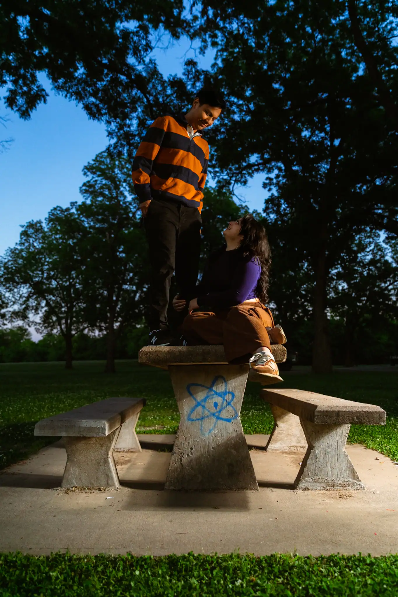 Young couple standing on park bench during sunset, enjoying each other's company.