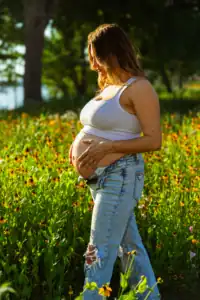 Pregnant woman standing in a vibrant flower field during golden hour.