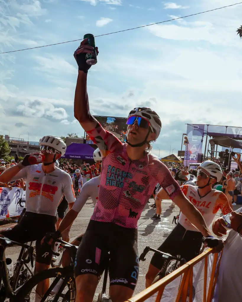 Cyclist raising a can in celebration among racers at a street race