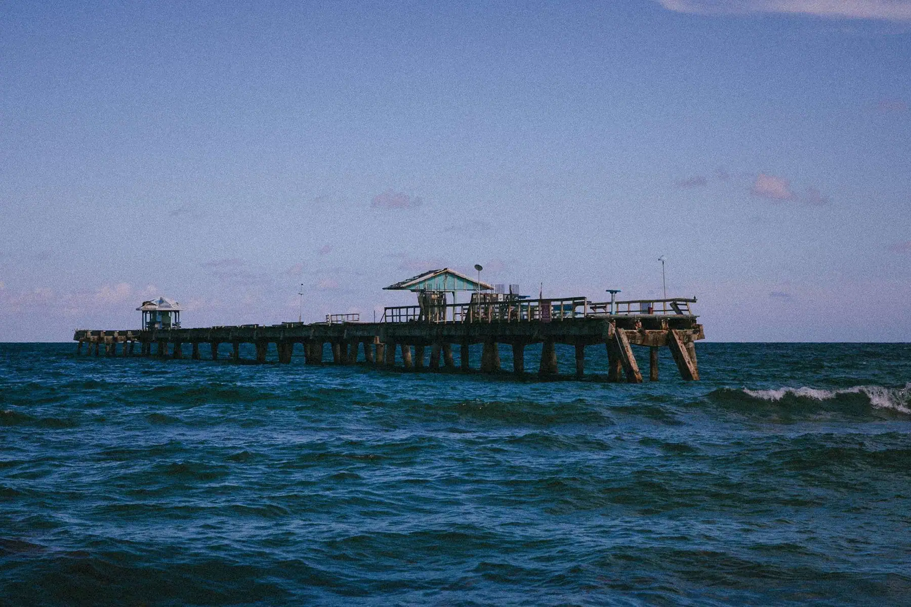 Weathered pier over blue ocean waves under a lavender sky
